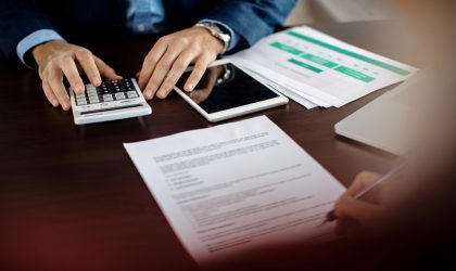 Close-up of financial consultant using calculator while his client is signing paperwork during the meeting.